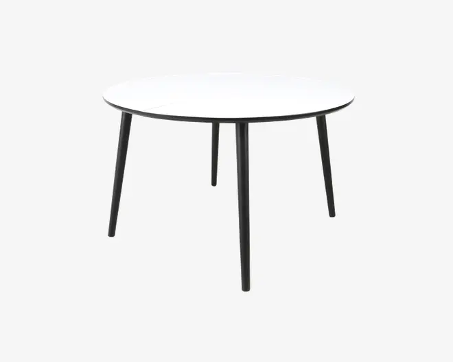 Et rundt bord med en glat, hvid bordplade og fire slanke, sorte metalben, der er let skråtstillede for stabilitet. Designet er minimalistisk og moderne med en tynd bordplade og et rent, enkelt udtryk.