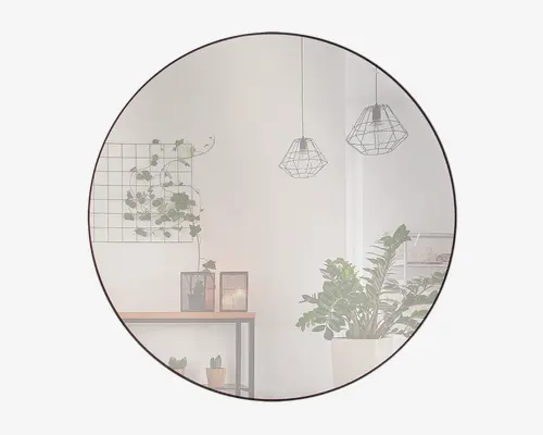 Stort, rundt vægspejl med en tynd, mørk ramme. Spejlet har en klar refleksion, der viser et moderne interiør med geometriske pendellamper, et konsolbord med dekorative lysestager og flere grønne planter. Designet er minimalistisk og moderne, velegnet til forskellige boligindretninger.
