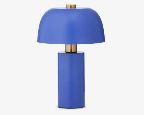 Moderne bordlampe med mat blå finish. Lampen har en cylindrisk fod og en kuppelformet skærm, begge i samme blå farve. Guld-farvede metaldetaljer ses øverst og mellem foden og skærmen. Minimalistisk design med glatte overflader og rene linjer.