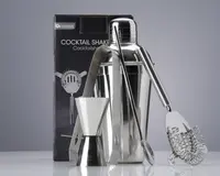 Et sæt barværktøj i rustfrit stål, herunder en cocktailshaker med blank overflade, en dobbeltsidet målebæger til væsker, en lang røreske, et par istænger og en cocktail-si med spiralformet fjeder. Produkterne er vist foran en mærket æske, og alle dele har et stilrent, moderne design, der passer til både hjemmebrug og professionel brug.