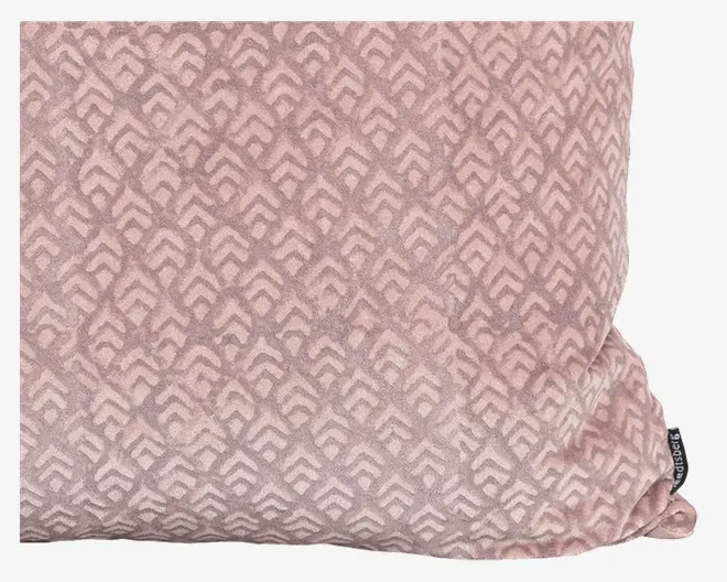 Rektangulær pude med en blød, velouragtig overflade i en afdæmpet rosa farve. Overfladen har et gentaget geometrisk mønster af sammenlåste chevroner i en lidt lysere nuance. Der sidder et lille stofmærke med branding i den ene side.