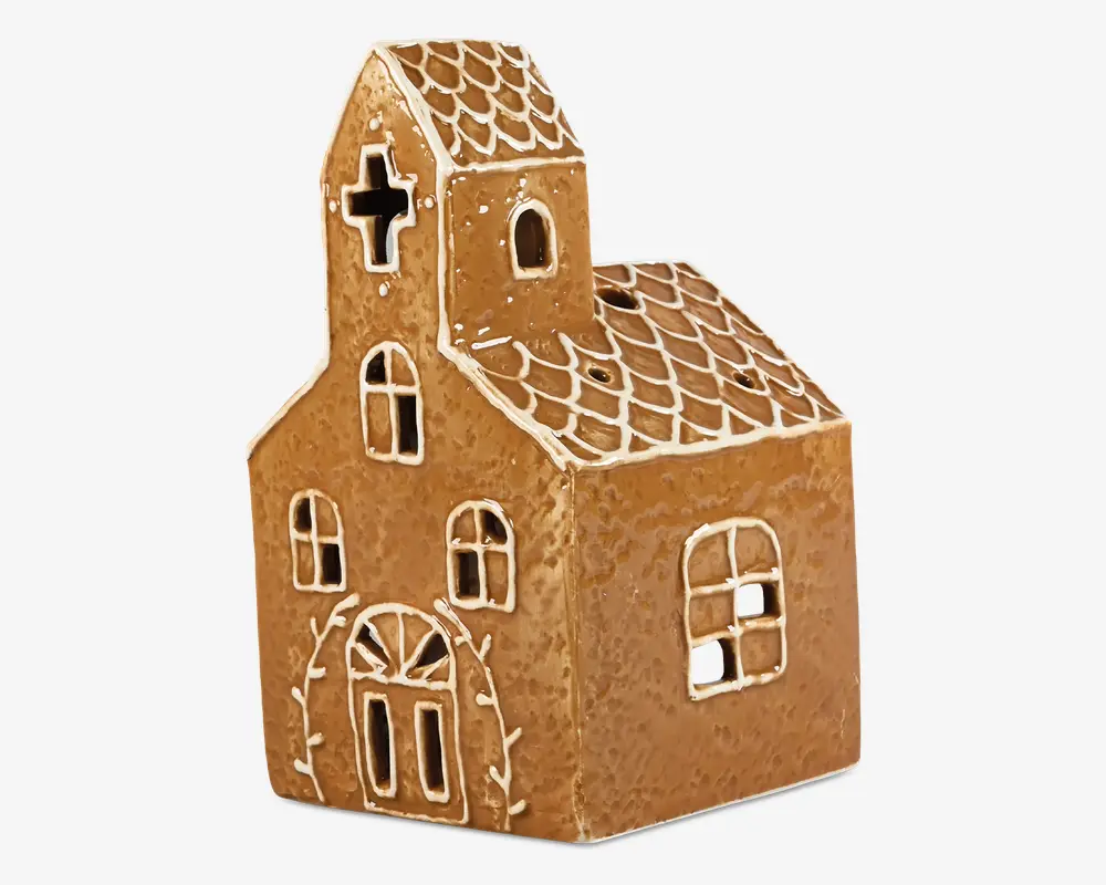 En dekorationsgenstand formet som en lille kirke, designet til at ligne honningkage med en brun, struktureret overflade og hvide glasur-lignende detaljer, der markerer vinduer, døre og tagsten. Forsiden har en dobbeltdør med et buet vindue over, to rektangulære vinduer og et tårn med et korsformet vindue. Siden har et stort kvadratisk vindue. Taget har et mønstret udseende, og helhedsindtrykket er festligt og charmerende, velegnet til julepynt.