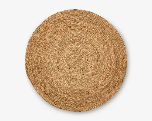 Rund vævet måtte lavet af naturlige jute-fibre med tæt flettet struktur og en varm, jordfarvet tan nuance. Måtten har en let ujævn kant, hvilket giver et rustikt og håndlavet udseende. Overfladen viser koncentriske cirkelmønstre, som er skabt af væveteknikken.