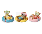 Tre dyrefigurer ligger afslappet på farverige baderinge. Hver figur har badebukser på og grønne briller med agurkeskiver over øjnene, hvilket giver et spa- eller afslapningstema. Den venstre figur ligner et surikat på en blå og rød badering, iført gule badebukser og holder en rød sodavandsdåse. Den midterste figur, delvist skjult af et sløret ansigt, ser ud til at være en dovendyr på en gul badering, iført blå badebukser og lyserøde hovedtelefoner. Den højre figur ligner en corgi-hund på en lyserød og blå badering, iført lyserøde badebukser og holder også en rød sodavandsdåse. Alle figurer har en afslappet og legende positur.