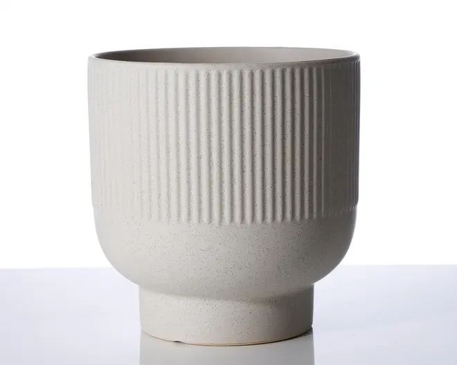 Et lysegråt keramikkar med mat finish. Den øverste halvdel har en lodret rillet tekstur, mens den nederste halvdel er glat og buer let indad, før den udvider sig ved foden. Formen er cylindrisk med et moderne, minimalistisk design.