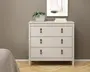 Et moderne, minimalistisk møbel med tre rummelige skuffer, hver med to brune læderstropper som greb for nem åbning. Kommoden har en glat, mat lysebeige finish og står på korte, solide ben. Toppen er dekoreret med en lille potteplante og en stak bøger, hvilket giver et dekorativt præg. Det samlede design er enkelt og stilrent, velegnet til moderne indretning.