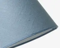 Nærbillede af en lampeskærm med klassisk konisk form, betrukket med lyseblåt tekstil med en let vævet struktur. Stoffet har en diskret mønster, og kanterne er pænt afsluttet med matchende blå kantbånd. Den indvendige foring er i en lys, neutral farve.