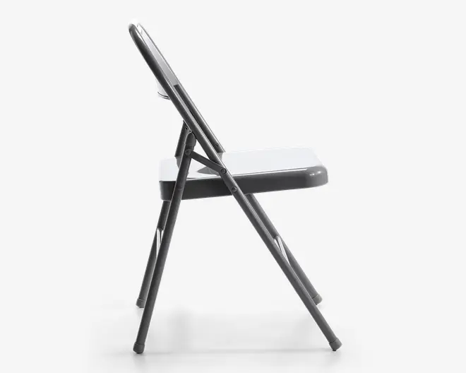 Sidebillede af en sammenklappelig stol i metal med et enkelt, minimalistisk design. Stolen har et fladt sæde og ryglæn, begge lavet af metal, samt rørformede metalben med plastikdutter for at beskytte gulvet. Foldemekanismen er synlig og viser solide hængsler og støttebøjler for stabilitet.