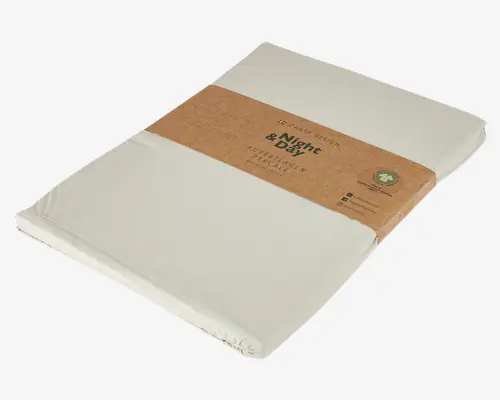 Et pænt sammenfoldet, lysebeige faconlagen med elastiske hjørner, pakket ind i et enkelt, miljøvenligt brunt papirbånd. Emballagen fremhæver det bæredygtige materiale og dansk design, med tydelig mærkning og et lille grønt emblem, der indikerer et miljøvenligt produkt.
