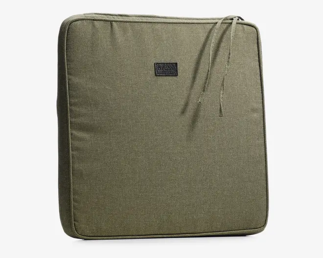 Firkantet pude med slidstærkt betræk i olivengrøn, der har en diskret vævet struktur. Puden har en kant med piping for ekstra form og to stofsnore i det øverste hjørne til fastgørelse på møbler. Foran er der påsyet et lille, rektangulært mærke, som giver et dekorativt præg.