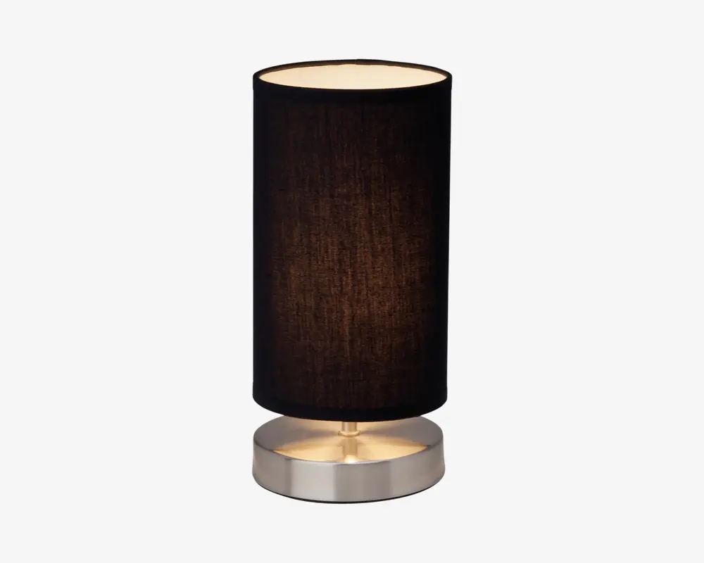 En moderne bordlampe med cylindrisk form, sort stofskærm og børstet metalfod. Lampen har et enkelt og minimalistisk design med en glat, rund fod og en lige, lodret skærm, der giver et blødt lys. Foden er lavet af metal med en diskret glans, som matcher den mørke skærm og giver et stilrent udtryk.