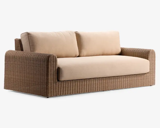 To-personers sofa med en robust ramme af flettet rattan i en naturlig brun farve. Sofaen har tykke, beige sæde- og ryghynder for ekstra komfort. Armlæn og bund er helt dækket af det samme flettede materiale, hvilket giver et ensartet og moderne udtryk, der egner sig til både indendørs og udendørs brug.