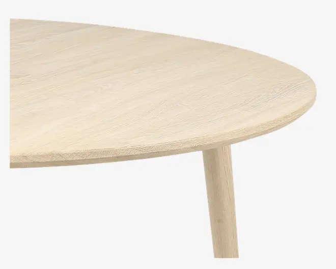 Nærbillede af et bord i lyst træ med en glat, afrundet kant og synlig træstruktur. Bordet har et enkelt, minimalistisk design med et cylindrisk ben.