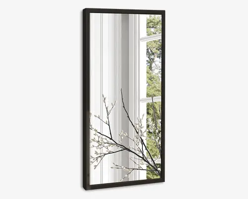 Rektangulært spejl med en slank, mørk ramme. Spejlet reflekterer et lyst interiør med hvide panelvægge, et stort vindue og en gren med små hvide blomster, hvilket giver en følelse af dybde og naturligt lys.