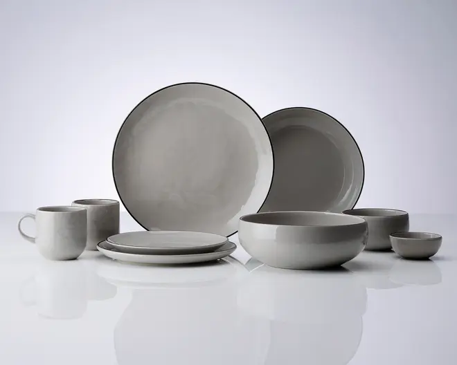 Et sæt stentøj i en blød grå farve med en let ujævn glasur. Sættet indeholder store middagstallerkener, mindre frokosttallerkener, dybe skåle, en lille skål og krus. Hver del har et minimalistisk design med glatte, afrundede kanter og en tynd, mørkere kant, der fremhæver formen. Udtrykket er moderne og enkelt, velegnet til både hverdags- og festbrug.