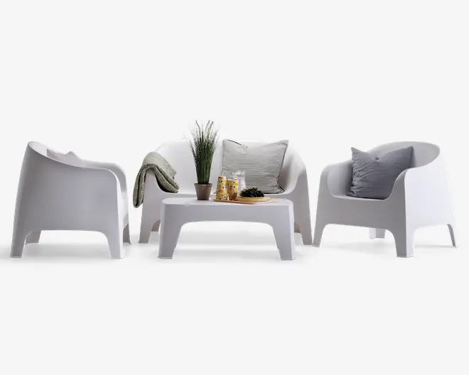 Moderne udendørs siddegruppe bestående af to armlæn-stole og en to-personers sofa, alle i en glat hvid finish. Sættet inkluderer et matchende lavt, rektangulært sofabord. Stolene og sofaen har blødt buede rygge og armlæn for komfort. Sofaen er pyntet med to grå puder og et tekstureret tæppe. Sofabordet er dekoreret med en potteplante, to glas, en tallerken med snacks og en lille skål, hvilket giver et hyggeligt og indbydende udtryk.