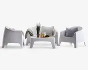 Moderne udendørs siddegruppe bestående af to armlæn-stole og en to-personers sofa, alle i en glat hvid finish. Sættet inkluderer et matchende lavt, rektangulært sofabord. Stolene og sofaen har blødt buede rygge og armlæn for komfort. Sofaen er pyntet med to grå puder og et tekstureret tæppe. Sofabordet er dekoreret med en potteplante, to glas, en tallerken med snacks og en lille skål, hvilket giver et hyggeligt og indbydende udtryk.