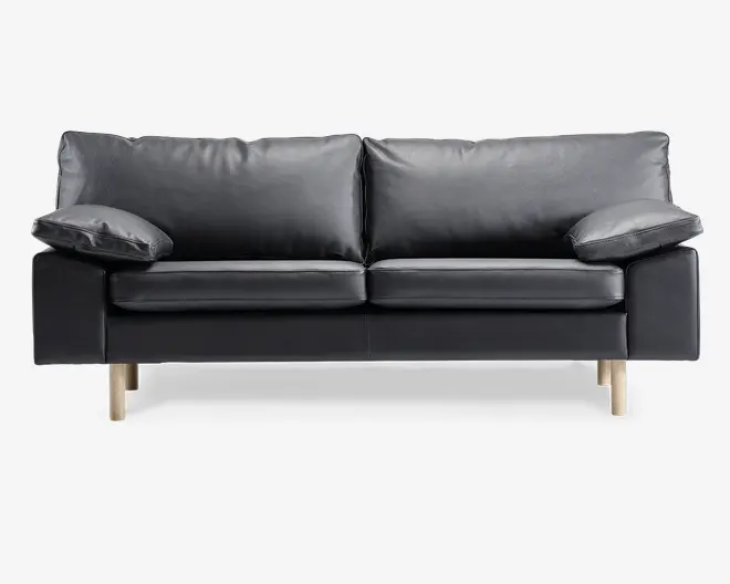En moderne sort lædersofa med to store sædehynder og to bløde ryghynder. Armlænene er brede og let skrå, hvilket giver ekstra komfort. Sofaen står på fire lyse træben, hvilket giver et moderne og let udtryk.