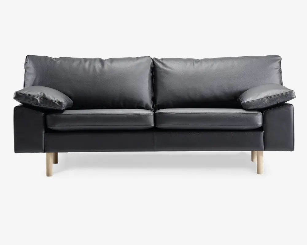 En moderne sort lædersofa med to store sædehynder og to bløde ryghynder. Armlænene er brede og let skrå, hvilket giver ekstra komfort. Sofaen står på fire lyse træben, hvilket giver et moderne og let udtryk.