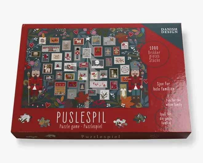 Æsken har et festligt design med et patchwork af små, farverige firkanter, der hver indeholder forskellige julemotiver som nøddeknækkere, hjerter, stjerner og juletræer. Baggrunden er dekoreret med kristtorn, bær og blade, hvilket giver et hyggeligt, sæsonpræget udtryk. Æsken angiver, at puslespillet indeholder 1000 brikker og er egnet til hele familien. Emballagen er overvejende rød med dekorative elementer og tydelig mærkning på flere sprog.