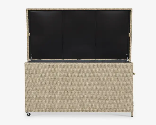 Rektangulær opbevaringskasse med flettet rattan-lignende ydre i en lys beige farve. Låget er åbent og afslører et rummeligt indre foret med sort materiale. Kassen har en solid konstruktion og står på små hjul for nem mobilitet. Låget holdes oppe af metalhængsler i begge sider.