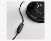 Nærbillede af en sort elektrisk ledning med en indbygget vippekontakt, der er forbundet til en robust, rund sort fod. Kontakten er nem at betjene med et enkelt tryk, og foden har en glat, blank overflade med en cirkulær fordybning for stabilitet.