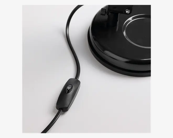 Nærbillede af en sort elektrisk ledning med en indbygget vippekontakt, der er forbundet til en robust, rund sort fod. Kontakten er nem at betjene med et enkelt tryk, og foden har en glat, blank overflade med en cirkulær fordybning for stabilitet.
