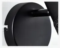 Nærbillede af et mat sort, cirkulært vægbeslag med glat overflade, synlig skrue i venstre side og et cylindrisk arm, der stikker ud. Designet er minimalistisk og moderne med rene linjer og et solidt udtryk.