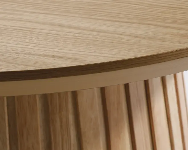 Nærbillede af en rund bordplade med en glat, lys træstruktur. Bordpladens kant er let affaset, og basen har lodrette, jævnt fordelte trælameller, hvilket giver et moderne og struktureret udtryk.