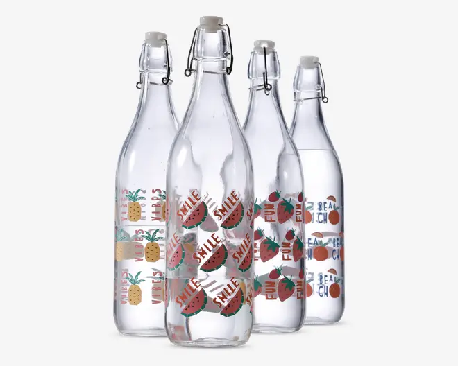 Sæt med fire klare glasflasker med patentlåg, hver med forskellige farverige frugtmotiver og sjove tekster. Én flaske har ananas og teksten 'VIBES', en anden har vandmelonskiver med 'SMILE', en tredje har jordbær med 'FUN', og den sidste har appelsiner med 'BEACH'. Flaskerne er høje og cylindriske, perfekte til servering af drikkevarer, og designet giver et muntert, sommerligt udtryk.