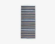 Rektangulært tekstil med skiftende horisontale striber i blå, brune, beige og hvide nuancer. Nogle striber har indviklede geometriske mønstre, herunder diamant- og zigzagmønstre. Enderne er afsluttet med korte hvide frynser.