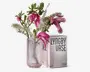 Klar cylindrisk vase i rillet glas med lyserøde blomster og hvide blomstergrene arrangeret i den, vist ved siden af emballagekassen mærket "LYNGBY VASE" og "20 cm".