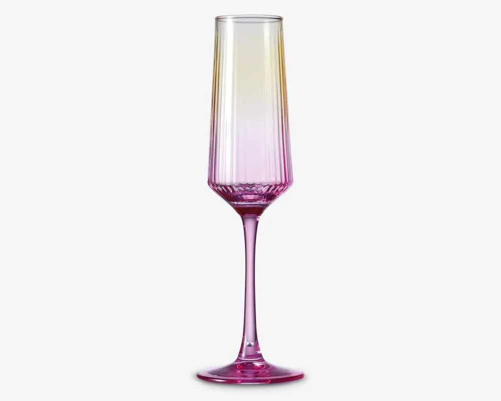 Høj, elegant glas med en rillet skål og en lang, slank stilk. Glasset har et farveforløb, der går fra gennemsigtigt øverst til en livlig pink bund. Skålen har lodrette riller, som giver struktur og et dekorativt udtryk. Foden og stilken er også farvet pink, hvilket giver glasset et moderne og stilfuldt look.
