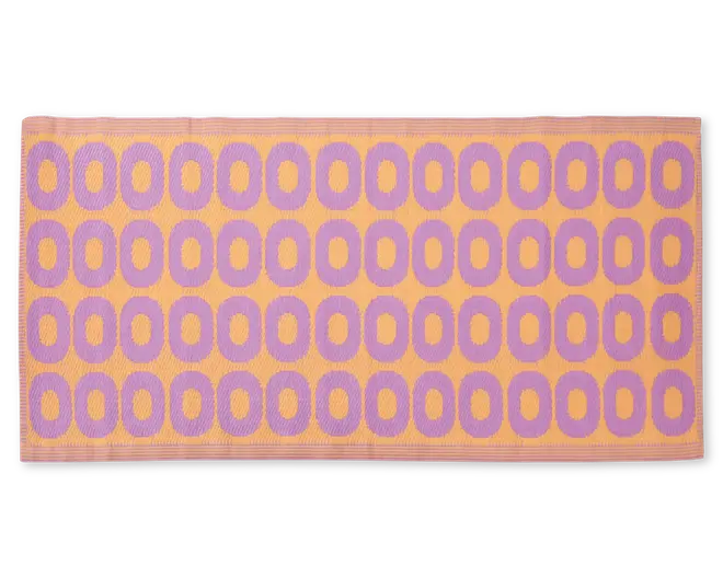 Rektangulært måtte med et gentagende mønster af lilla ovale former arrangeret i rækker på en ferskenfarvet baggrund. Måtten har en tekstureret overflade og en ferskenfarvet kant rundt om kanterne.
