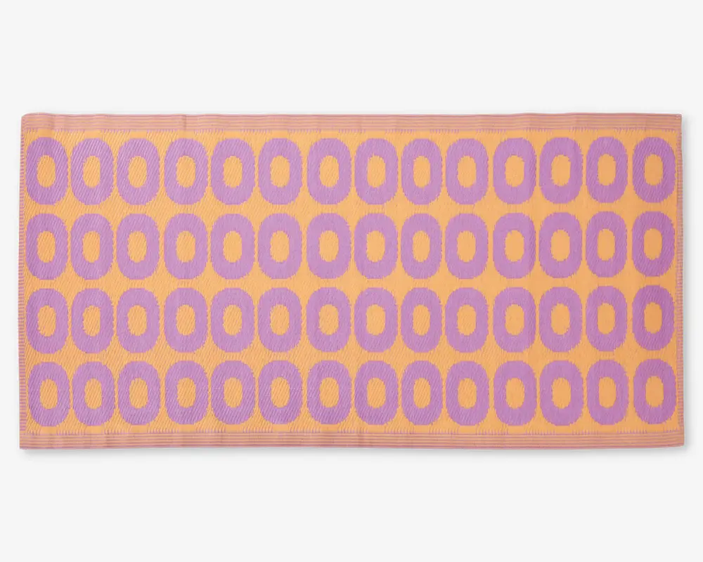 Rektangulært måtte med et gentagende mønster af lilla ovale former arrangeret i rækker på en ferskenfarvet baggrund. Måtten har en tekstureret overflade og en ferskenfarvet kant rundt om kanterne.