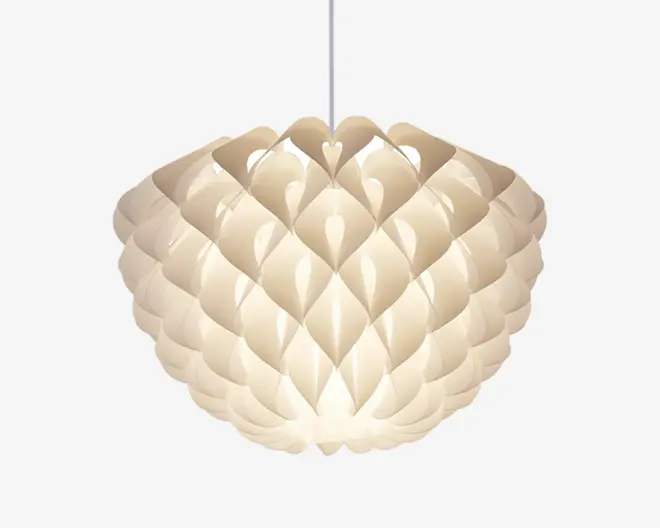 En pendellampe med et skulpturelt, lagdelt design, der ligner overlappende kronblade eller skæl. Skærmen er lavet af sammenlåste, buede stykker af uigennemsigtigt materiale, hvilket giver et blødt, diffust lys. Formen er rund og organisk med et moderne og dekorativt udtryk. Lampen hænger fra en central ledning.