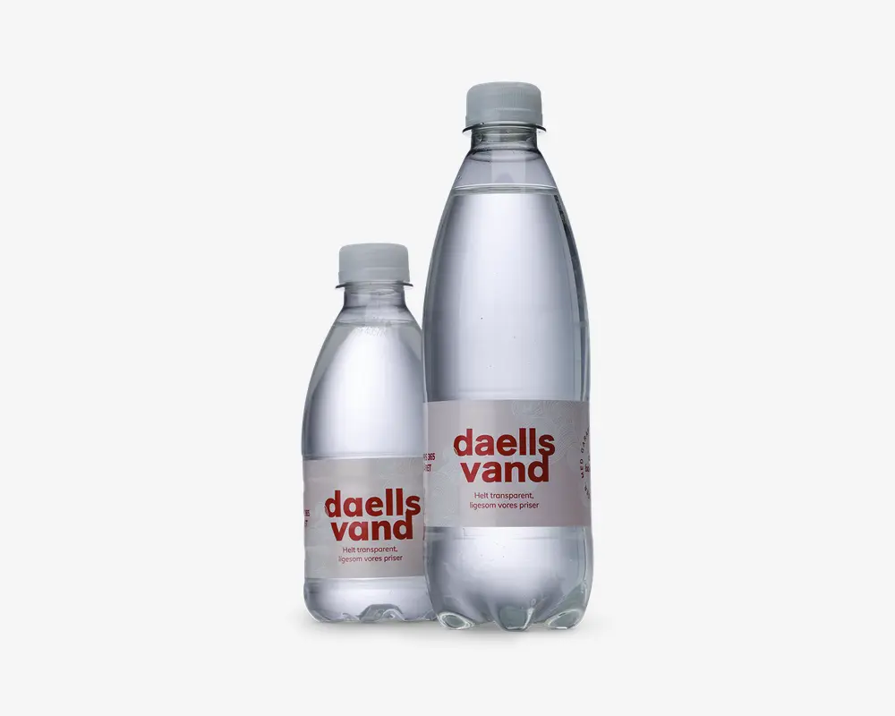 To klare plastflasker med skruelåg, én mindre og én større, begge fyldt med vand. Hver flaske har en enkel, gennemsigtig etiket med rød, fed tekst og minimalistisk design. Flaskerne har en glat, cylindrisk form, og etiketterne viser mærkenavnet tydeligt.