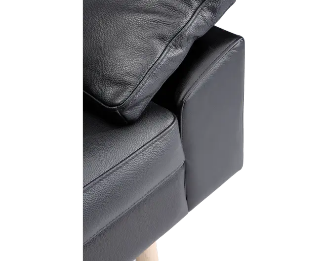 Nærbillede af et sofahjørne med sort tekstureret læderbetræk, en blød sædepude, en matchende ryghynde og en polstret armlæn. Sofaen har lyse træben, som kan ses nederst.