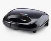 En kompakt, sort maskine med buet top og integreret håndtag for nem åbning. På toppen er der to indikatorlamper – en rød og en grøn – som viser strøm- og klarstatus. Apparatet har en sikker lås foran og står på fire små fødder for stabilitet. Den har en glat, blank overflade, der giver et moderne udseende.