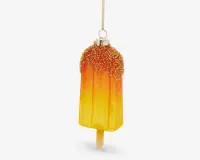 Et dekorativt ornament formet som en ispind, med en farvegradient fra gul til orange. Den øverste del er dækket af glitrende, teksturerede krymmel, og der er en metallisk hætte og løkke til ophængning. Ornamentet har en realistisk ispind i bunden.