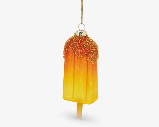 Et dekorativt ornament formet som en ispind, med en farvegradient fra gul til orange. Den øverste del er dækket af glitrende, teksturerede krymmel, og der er en metallisk hætte og løkke til ophængning. Ornamentet har en realistisk ispind i bunden.
