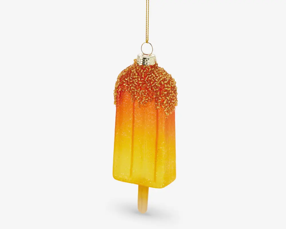Et dekorativt ornament formet som en ispind, med en farvegradient fra gul til orange. Den øverste del er dækket af glitrende, teksturerede krymmel, og der er en metallisk hætte og løkke til ophængning. Ornamentet har en realistisk ispind i bunden.