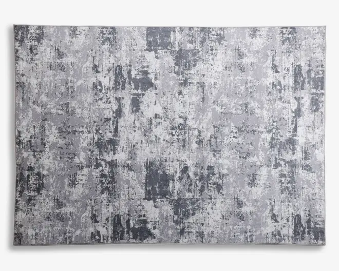 Rektangulært tekstil med et moderne abstrakt mønster i forskellige grå nuancer, der har et slidt og tekstureret udtryk. Designet består af uregelmæssige felter og penselstrøgslignende markeringer, hvilket giver et moderne og alsidigt udseende, der passer til mange indretninger.