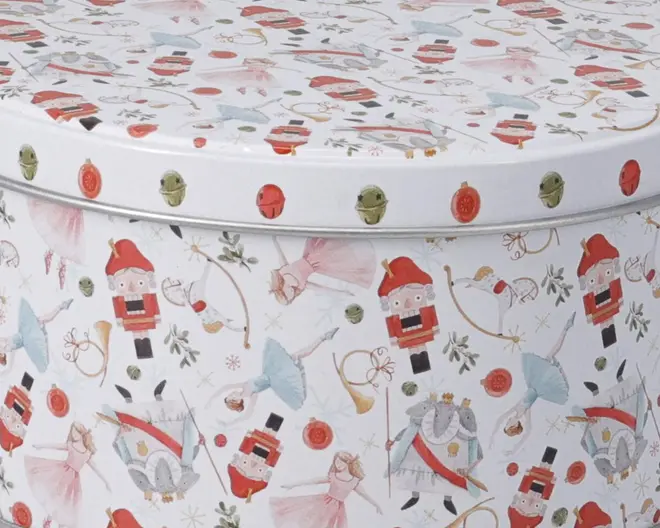 Overfladen har et festligt mønster med illustrationer af nøddeknækkere, ballerinaer i pastelfarvede dragter, en konge i kongeligt tøj, trompeter, julekugler og kristtjørn. Designet bruger bløde farver som rød, blå, grøn og guld, hvilket giver et eventyrligt og julet udtryk. Motiverne er jævnt fordelt og gentaget over hele det synlige område, hvilket skaber et legende og dekorativt udseende.