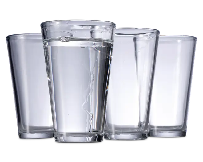 Sæt med fire klare, cylindriske drikkeglas med let konisk form, bredere foroven og smallere forneden. Glassene har en glat overflade og en tyk, solid bund for stabilitet. Ét glas er fyldt med vand, mens de tre andre er tomme.