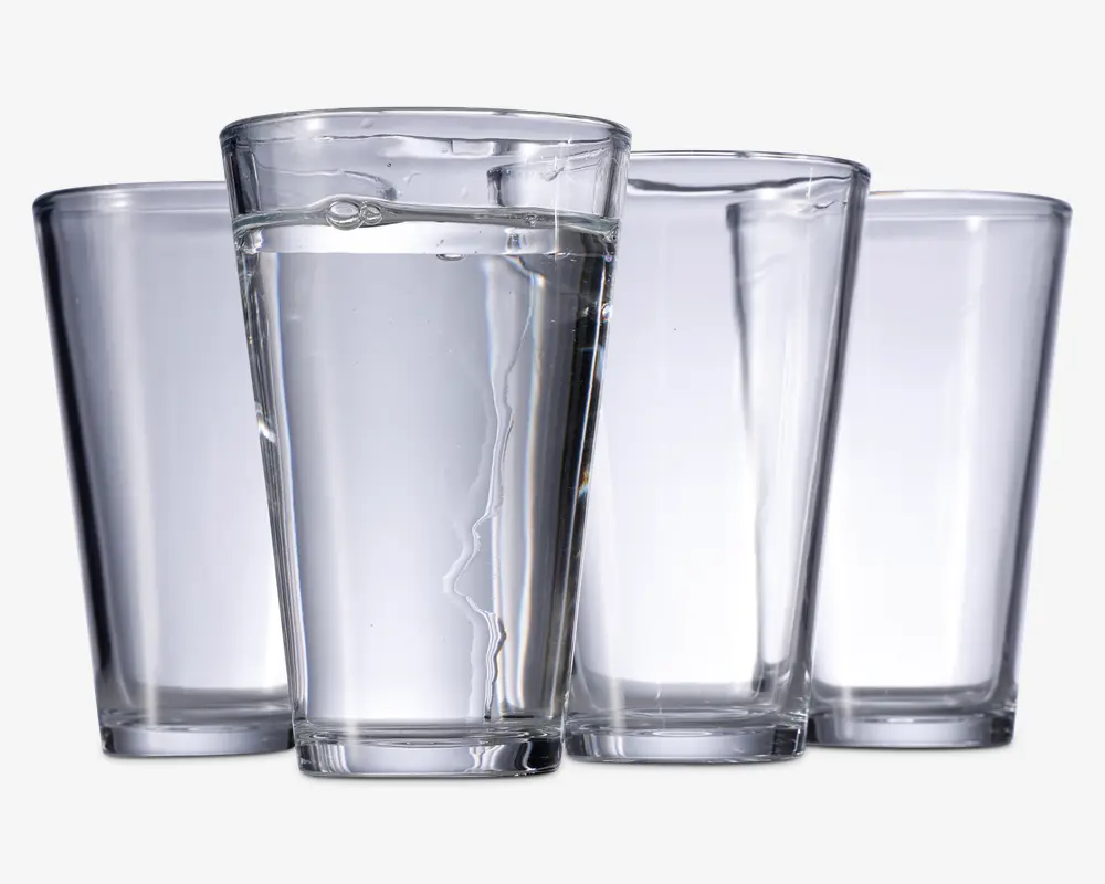 Sæt med fire klare, cylindriske drikkeglas med let konisk form, bredere foroven og smallere forneden. Glassene har en glat overflade og en tyk, solid bund for stabilitet. Ét glas er fyldt med vand, mens de tre andre er tomme.