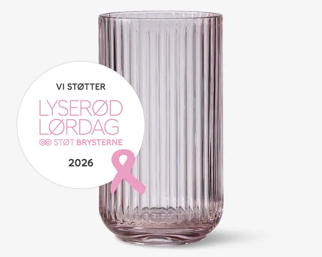Højt, klart glas med lodret rillet struktur, en svag rosa tone og afrundet bund. Et rundt mærkat på forsiden viser dansk tekst om støtte til brystkræft, sammen med en lyserød sløjfe og året 2026.