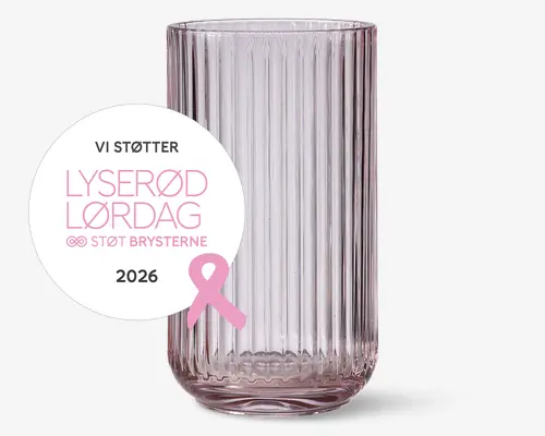 Højt, klart glas med lodret rillet struktur, en svag rosa tone og afrundet bund. Et rundt mærkat på forsiden viser dansk tekst om støtte til brystkræft, sammen med en lyserød sløjfe og året 2026.