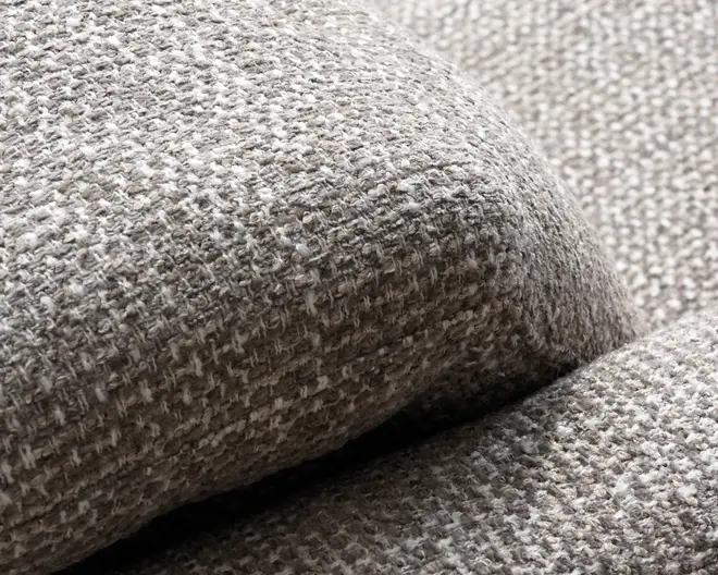 Nærbillede af et grå-beige vævet stof med en blød, nubret bouclé-lignende struktur og tykke polstrede kurver.