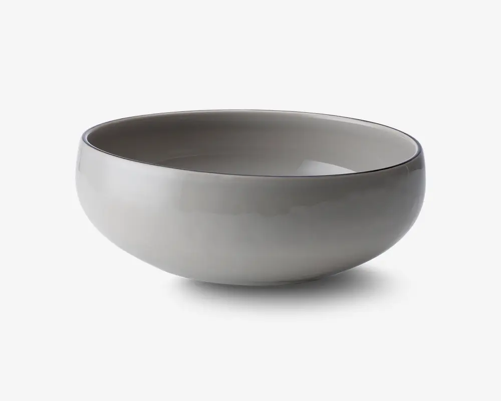 En rund, glat skål med blank lysegrå yderside og inderside. Skålen har et enkelt, minimalistisk design med blødt buede sider og en let tyk kant. Den ser ud til at være lavet af keramik eller porcelæn og er velegnet til servering af suppe, salat eller andre retter.